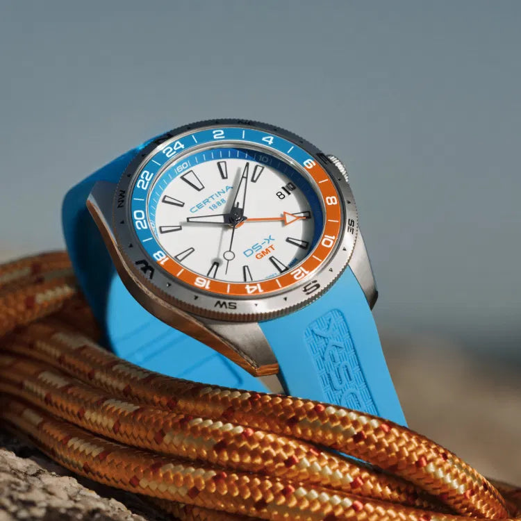 Close-up of the Certina DS-X GMT C047.452.17.011.00 lying on a climbing rope, showing the white dial, orange and blue 24-hour bezel, and blue rubber strap with DS-X logo embossing.