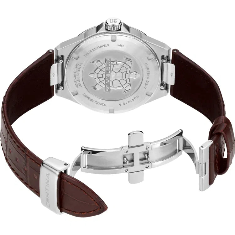 The Certina DS-7 Quartz watch positioned on its side, showing the stainless steel case back with the embossed Certina turtle emblem. The brown leather strap is partially open, revealing its rich texture, visible stitching, and a polished stainless steel butterfly clasp with a "Certina" engraving. The case back engravings include details such as "Certina DS-7," reference number "C043.410 A," "Stainless Steel," "Sapphire Crystal," and "Water-Resistant 10 bar (100m/330ft)." The crown, engr