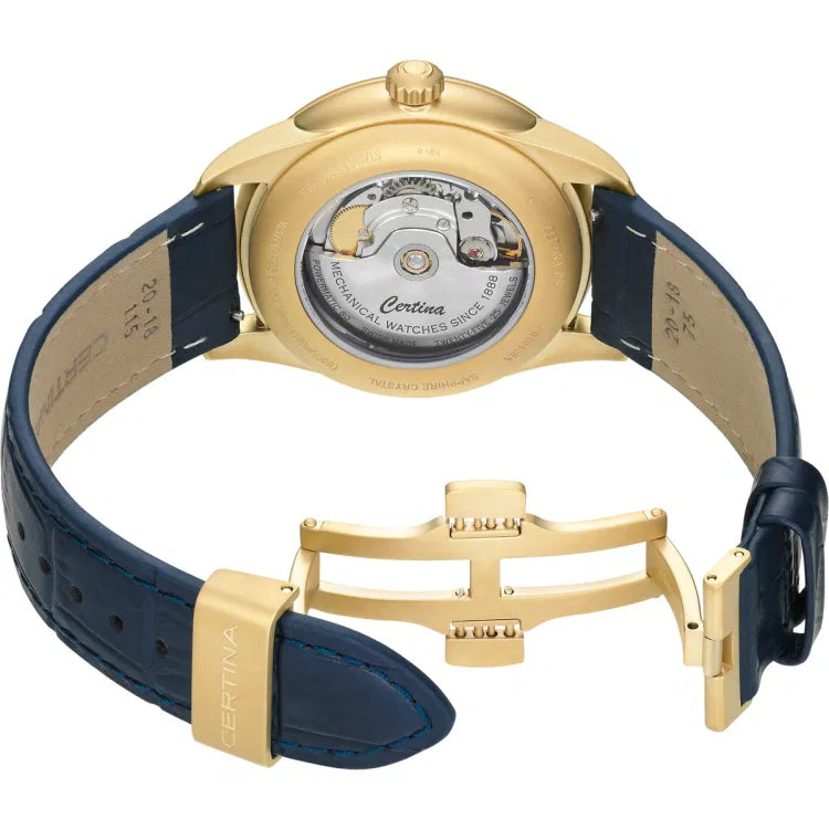 Close-up rear view of the Certina DS-1 Big Date Powermatic 80 with open butterfly clasp, showing the transparent case back and Powermatic 80 automatic movement engraved with “Certina”, “Mechanical Watches Since 1888”, and “TWENTY-FIVE 25 JEWELS”. The gold-tone PVD case and clasp pair with a blue leather strap, marked inside with “20–18 115” for width and length specifications.