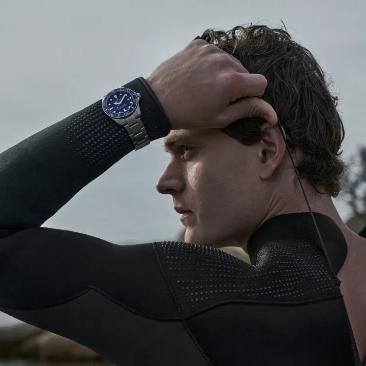 A diver wearing the Certina DS Action Diver 40.5mm titanium watch over a black wetsuit, pulling on a wetsuit cord. The blue dial and ceramic bezel are clearly visible on the wrist, highlighting the watch’s sporty and professional dive-ready design.