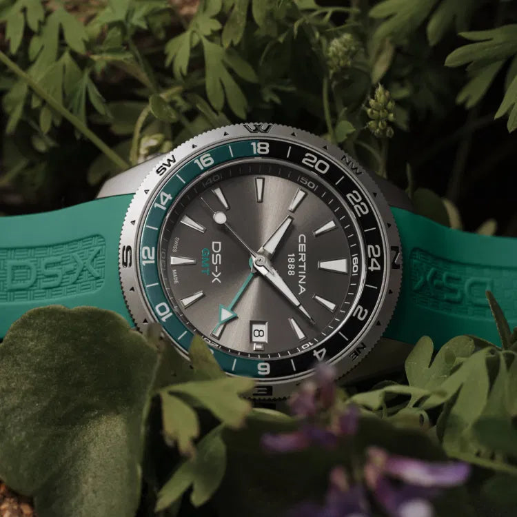 certina ds-x gmt c047.452.17.081.00 in close-up with green rubber strap and grey dial, visible certina 1888 and ds-x gmt logos, black-green gmt bezel, swiss made watch photographed in forest vegetation