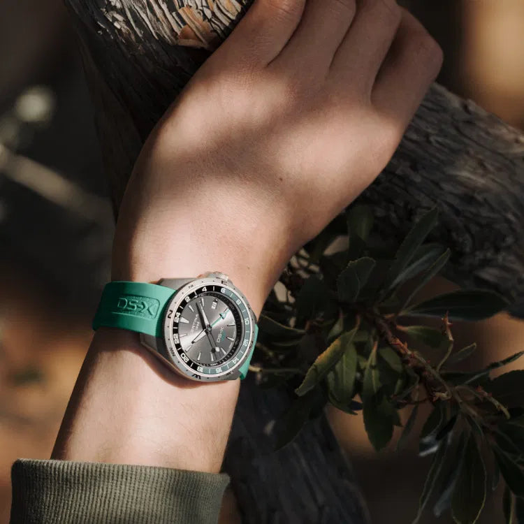 certina ds-x gmt c047.452.17.081.00 with grey dial and green rubber strap, worn outdoors on wrist, showing green-black gmt bezel, certina 1888 and ds-x gmt logo, swiss made sports watch in nature