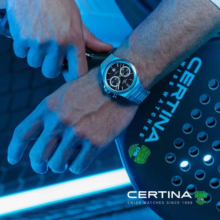 A man wearing the Certina DS-7 Chrono Auto C043.427.21.051.00 in an action setting, featuring a black dial with chronograph subdials. The PVD-coated stainless steel case and bracelet enhance the sporty yet elegant look. The blue-lit sports environment in the background reinforces the watch’s dynamic appeal, with Certina branding visible in the lower corner.