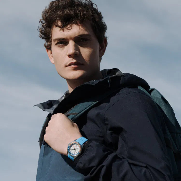 Man wearing Certina DS-X GMT C047.452.17.011.00 watch with blue rubber strap, white dial, and red-blue 24-hour bezel, standing outdoors in daylight.