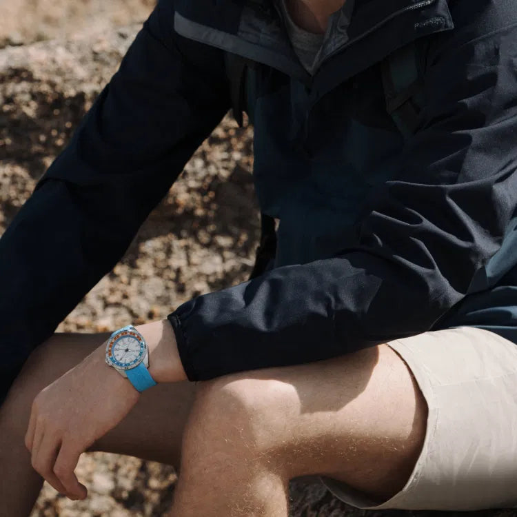 Man seated on a rock, wearing the Certina DS-X GMT C047.452.17.011.00 with a blue rubber strap, white dial, and red-blue bezel, visible on his left wrist.