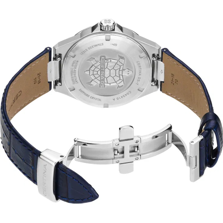 Side-angled view of the Certina DS-7 Quartz watch showcasing its stainless steel case and engraved case back with the Certina turtle emblem. The dark blue leather strap is fully extended, displaying its smooth beige underside, blue stitching, and stainless steel butterfly clasp. The watch’s engravings highlight details such as 'Certina DS-7,' water resistance up to 100 meters (10 bar), and sapphire crystal construction.